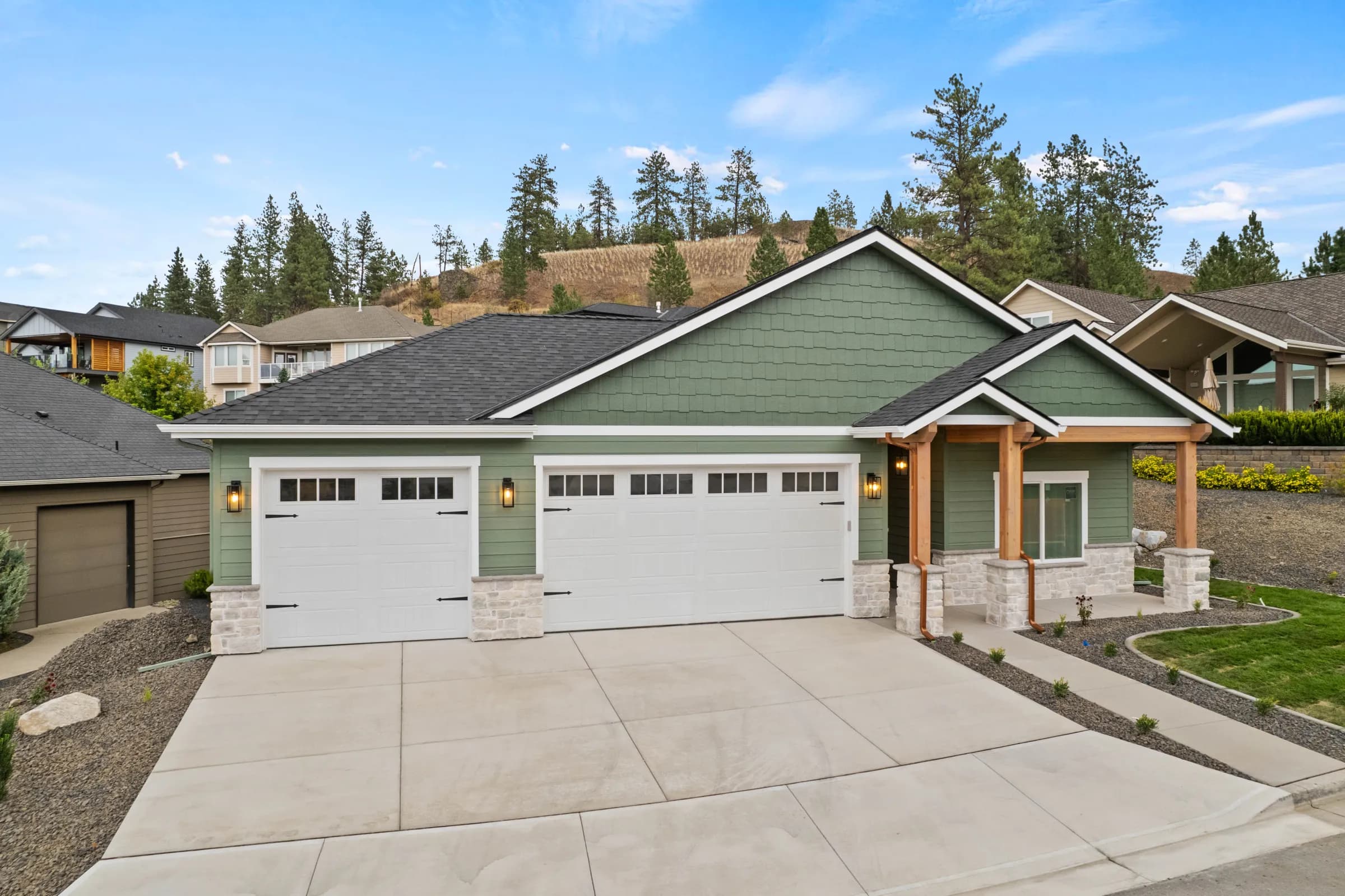 Sage-green craftsman by JM Homes with a timber-framed entry and three-car garage