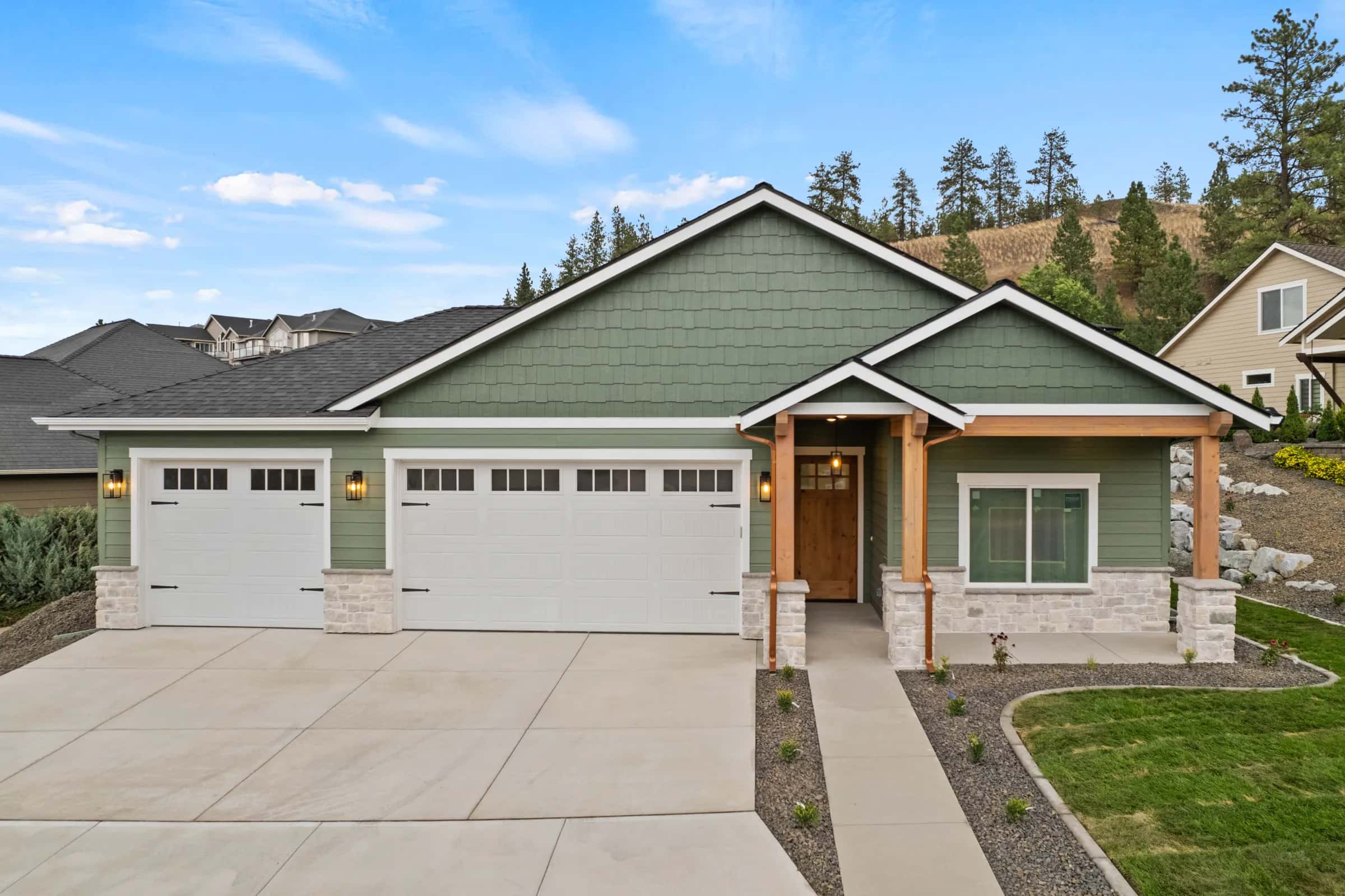 Sage-green craftsman by JM Homes with a timber-post porch and three-car garage