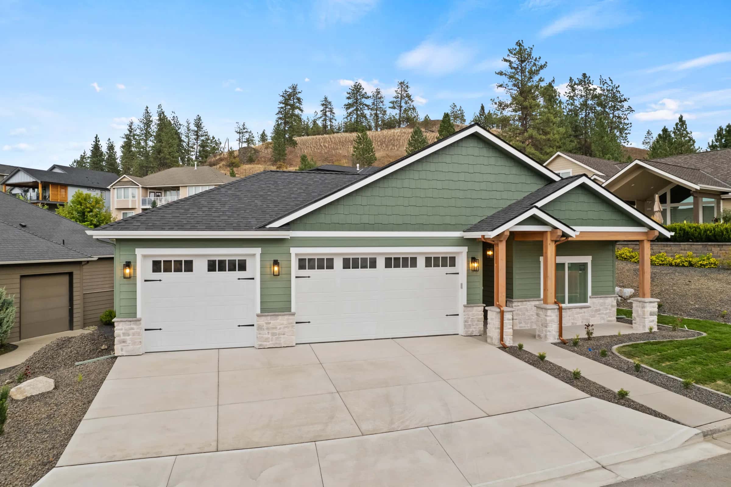 Green craftsman with stone accents and a wide concrete drive