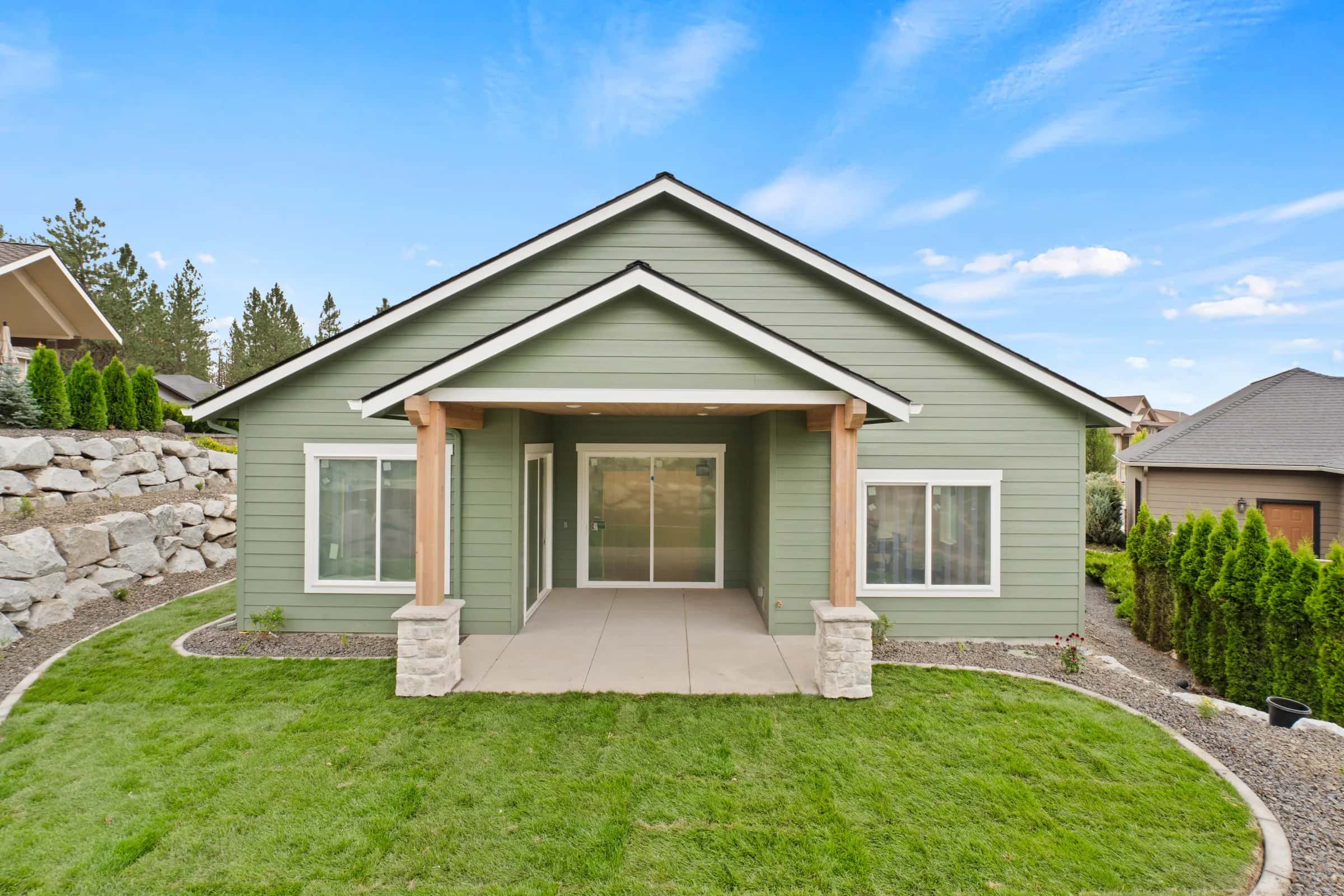 Rear of a sage-green craftsman with a timber-post covered patio and lawn