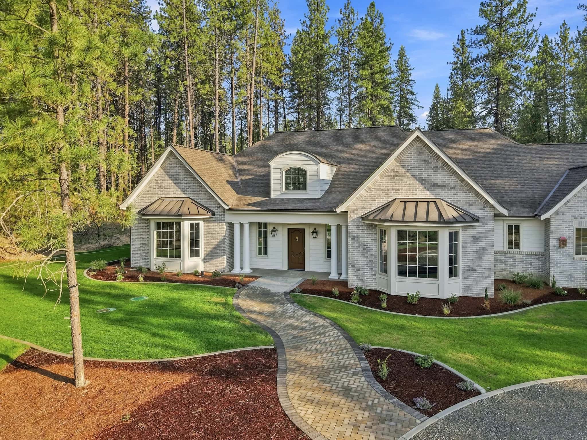 Painted-brick French country home by JM Homes with a curving paver walk among tall pines