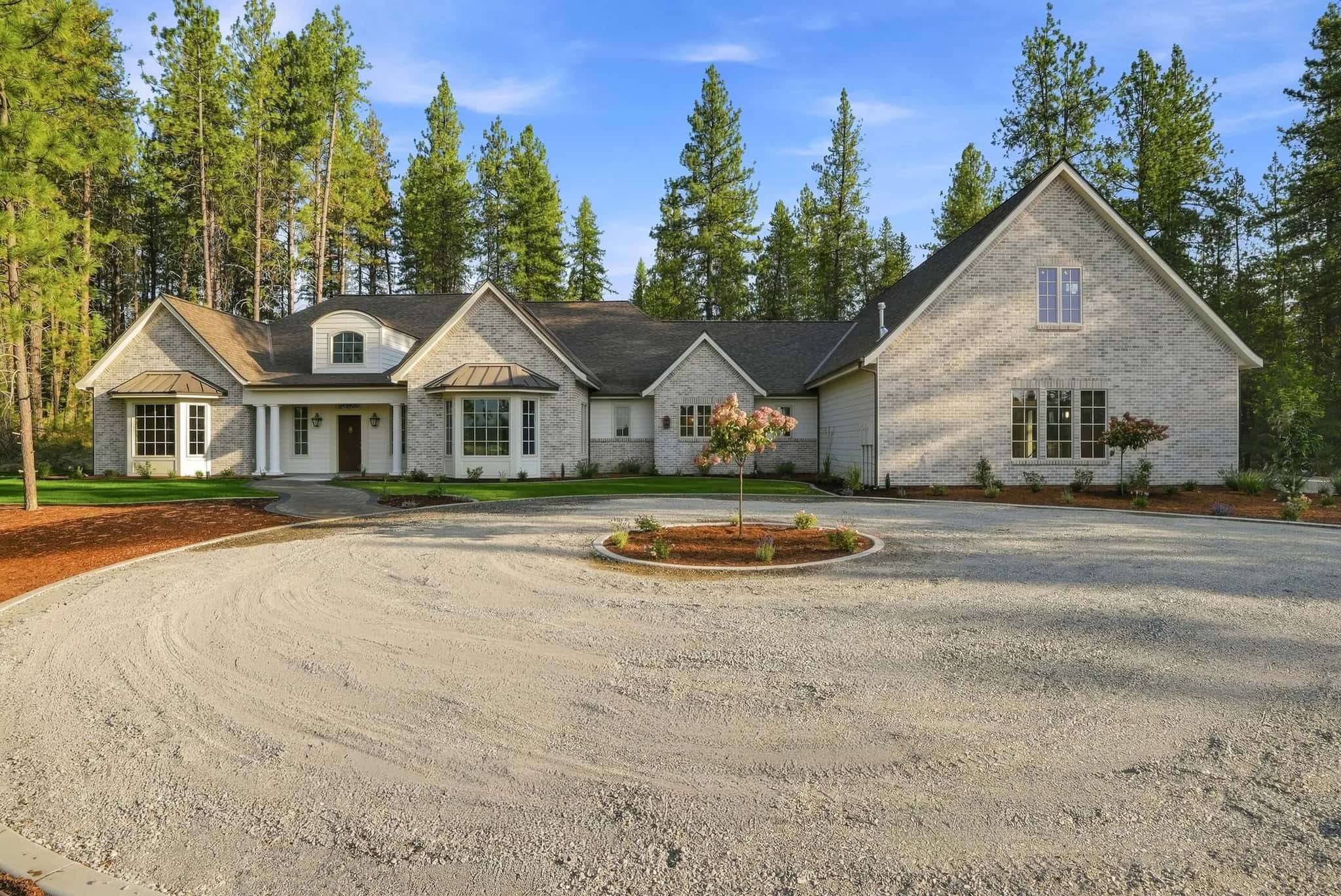Brick home by JM Homes with a columned porch and circular drive among tall pines