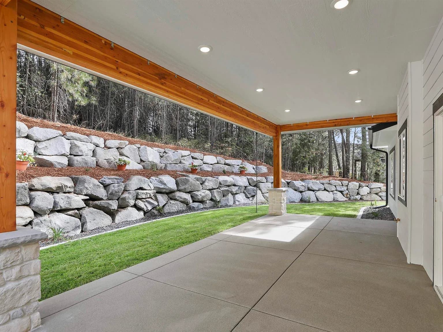 Covered back patio with timber beams opening onto the yard and pines